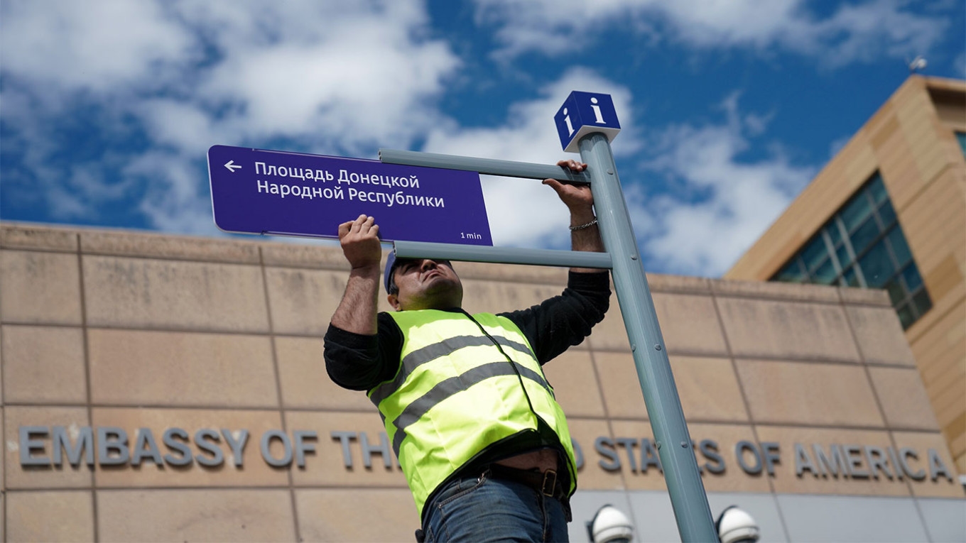 Фото: рабочий устанавливает дорожный знак около посольства США в Москве, с июня 2022-го территория перед зданием носит название «площадь Донецкой Народной Республики» / АГН «Москва»