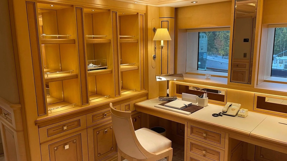 Кабинет владельца яхты, каюта для работы. На полке стоит макет арестованной «Шахерезады». На фото также видно судно с эмблемой ФСБ за окном, а на столе — телефон спецсвязи без кнопок и с гербом.