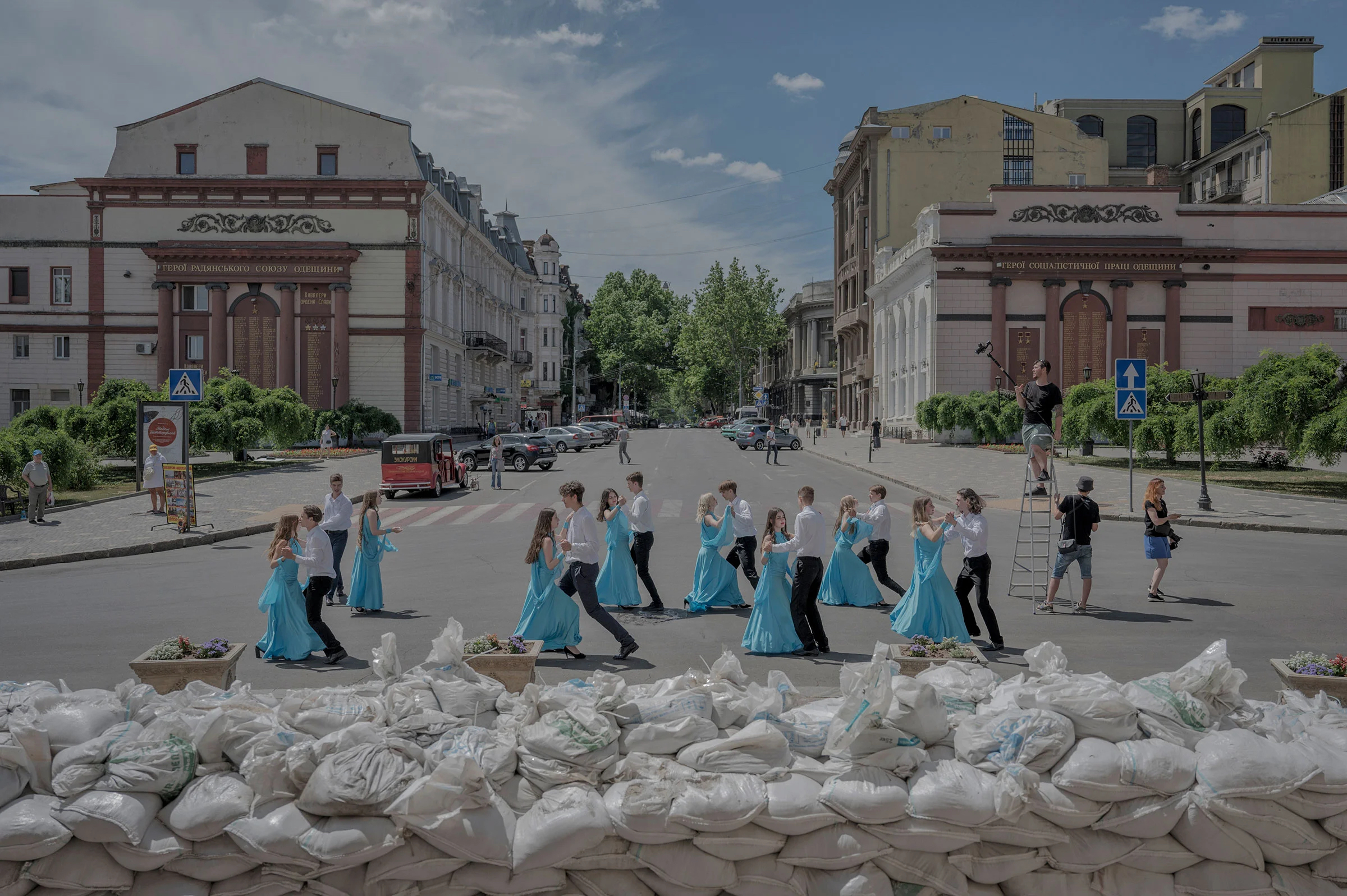 Выпускники школы танцуют у мешков с песком, защищающих фасад оперного театра в Одессе, 15 июня